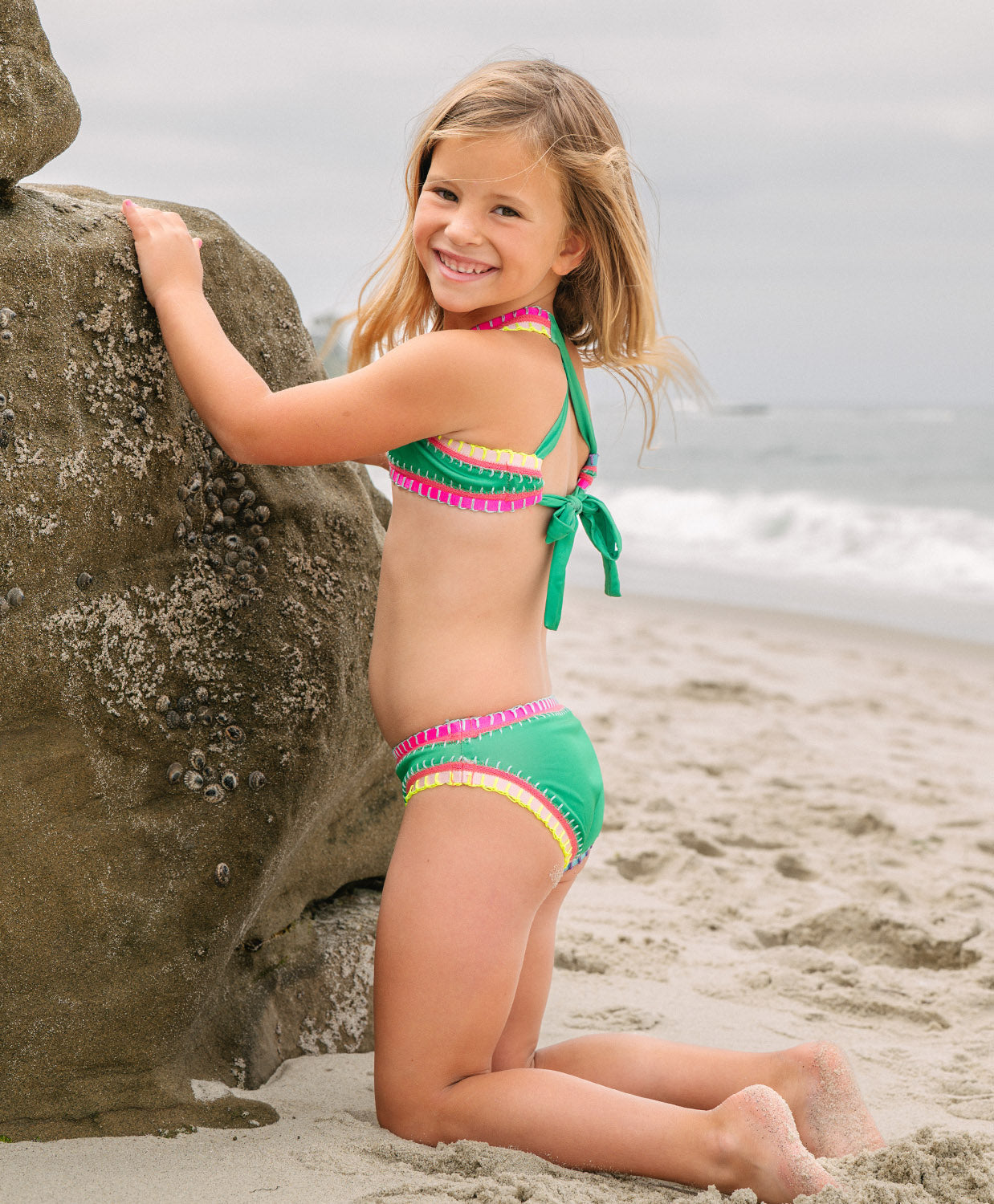 Meisje in groene bikini zittend op het strand