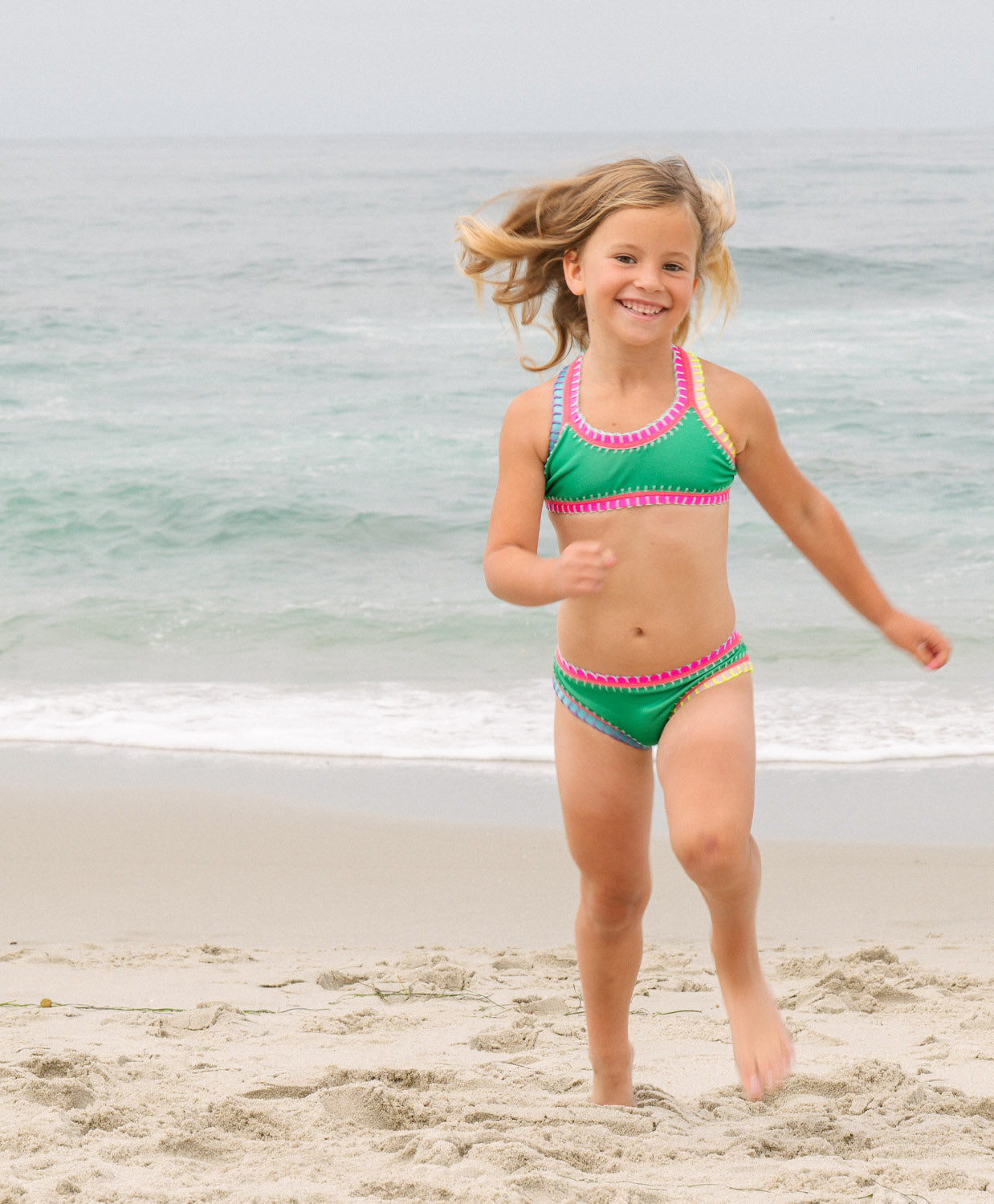 Meisje in groen roze PQ Swim bikini rennen op strand